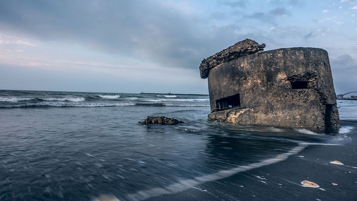 １座頹圮碉堡傾落在沙灘上，一波波的海浪正拍打著它。（圖片來源：瑞貝卡一家）