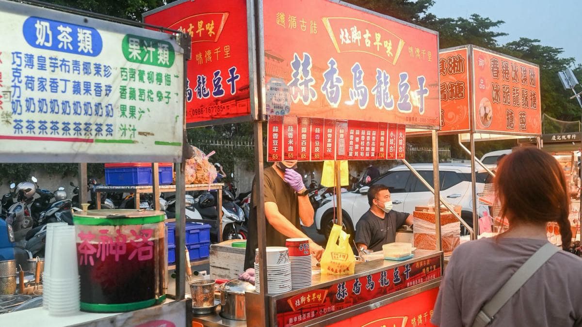 灶腳古早味蒜香烏龍豆干就在精誠夜市停機車的那條圍牆邊。（圖片來源：阿君的玩食天堂）